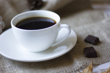 A cup of coffee and some chocolate with autumn leaf on the foreground.