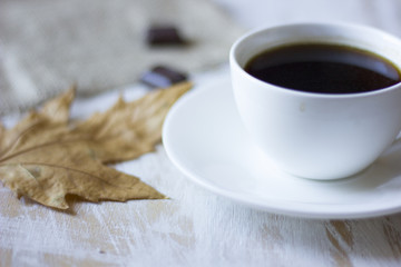 A cup of coffee and some chocolate with autumn leaf on the foreground.