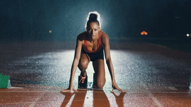  Female athlete training at running track in the dark & in the rain. Slowmo