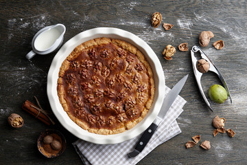 Traditional walnut pie, spices, nuts and nutcracker on dark wooden table, top view