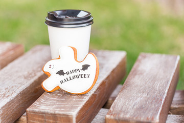 Halloween homemade gingerbread and honey cookies  as a white ghost with happy halloween greetings text on a wooden bench and cup of coffee on the background