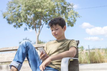 Obraz premium Schoolboy on bench taking break using mobile