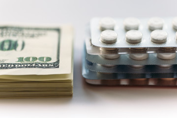 Bundle of money and  pack of medication tablets or drug pills, close-up. Expensive health care concept