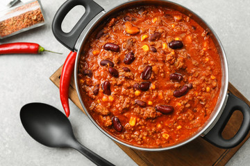 Saucepan with delicious chili con carne on wooden board