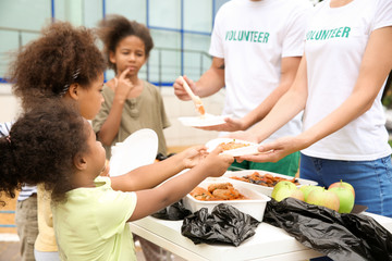 Volunteers sharing food with poor African children outdoors - obrazy, fototapety, plakaty