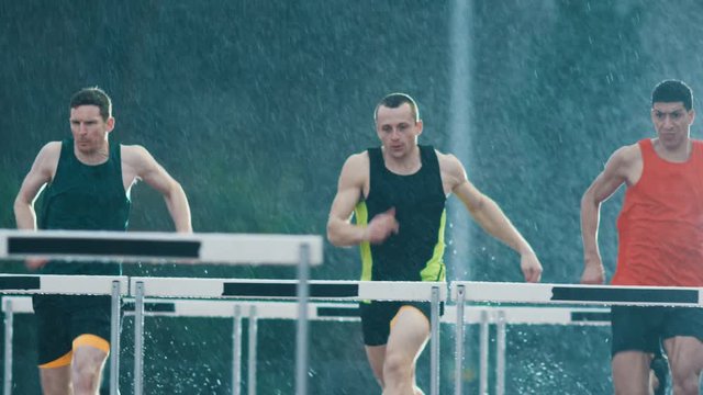  Athletes running & jumping over hurdles at athletics track in the rain