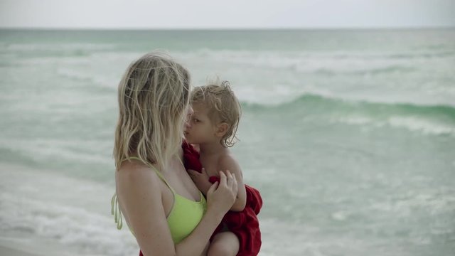 Mother holding son on her hand on the shore of the beach. Smiling woman pick up her little boy, kiss and hug 4k