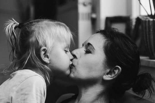 toddler with long blond hair  kissing his mom gently on her lips