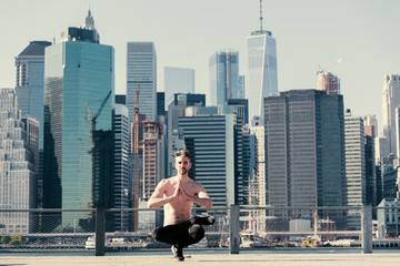 Man doing a lifted lotus yoga toe stand in front of the Manhattan skyline.