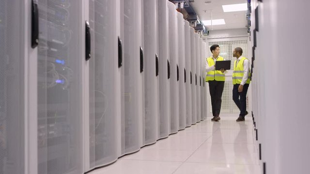 Data administrators walking between rows of server racks and checking the machines.