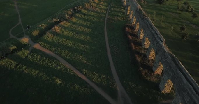 Video from above. Aerial view of the ancient Roman Aqueduct at sunset. Old ruins surrounded by a green public Park (Parco degli Acquedotti) Rome, Italy.