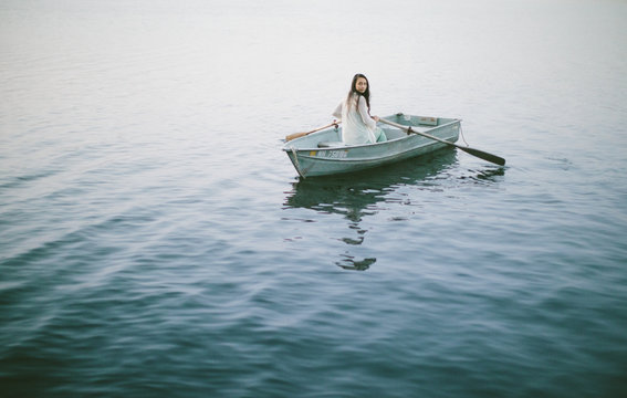 Lonely girl floats alone in a row boat on a foggy New England morning.