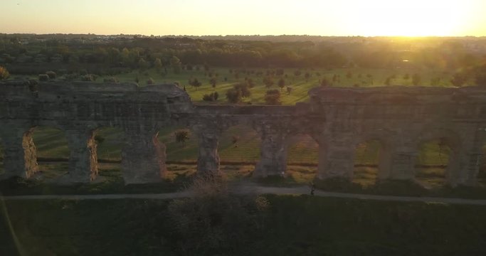 Video from above. Aerial view of the ancient Roman Aqueduct at sunset. Old ruins surrounded by a green public Park (Parco degli Acquedotti) Rome, Italy.