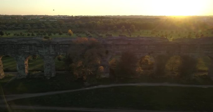 Video from above. Aerial view of the ancient Roman Aqueduct at sunset. Old ruins surrounded by a green public Park (Parco degli Acquedotti) Rome, Italy.