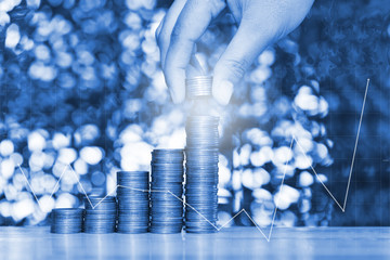 Double exposure of woman hand put coin on step of coins stacks on table with financial graph chart, for saving banking finance concept.