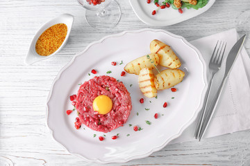 Delicious steak tartare with yolk, pomegranate seeds and potatoes on plate