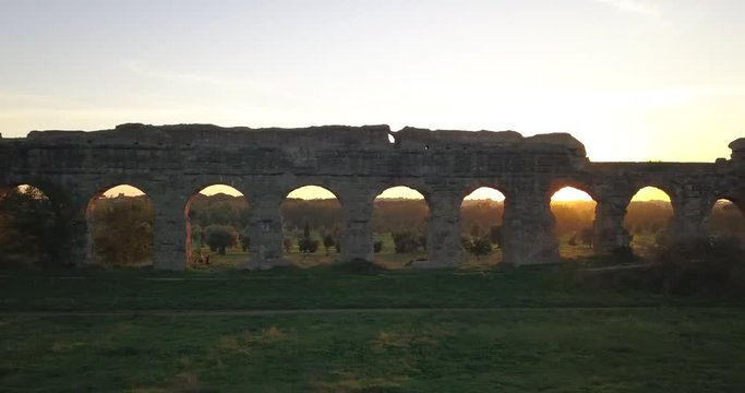 Video from above. Aerial view of the ancient Roman Aqueduct at sunset. Old ruins surrounded by a green public Park. Rome, Italy.