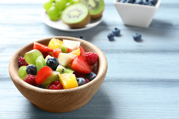 Bowl with delicious fruit salad on wooden background