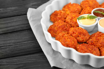 Baking dish with tasty sausage balls and sauces on table