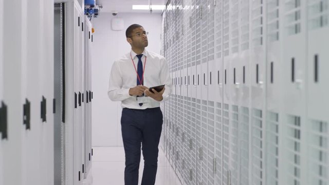 IT engineer with computer tablet checking the rows of server racks in a data center.