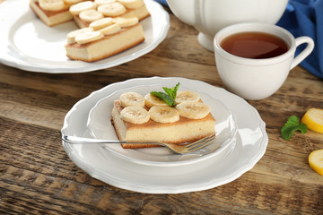 Plate with tasty banana cake and cup of tea on wooden table