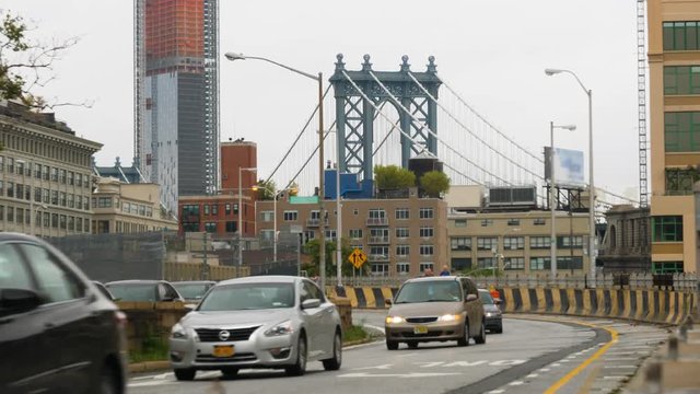 A daytime overcast establishing shot of traffic leaving the Brooklyn Bridge on the Brooklyn side. The Manhattan Bridge is in the distance.  	