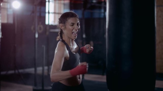 Powerful female boxer training with punch bag in urban gym