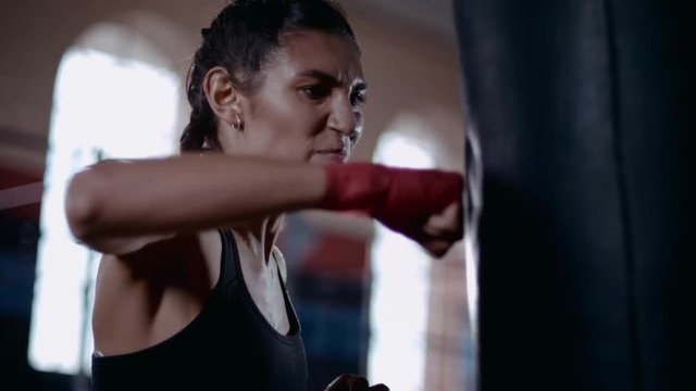  Powerful female boxer training with punch bag in urban gym. Super slow motion