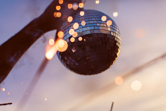 A person holding up a disco ball at the beach