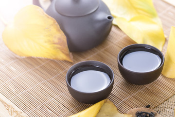 Black teapot and cups with yellow leaves on the table. Hot drinks. Autumn tea.