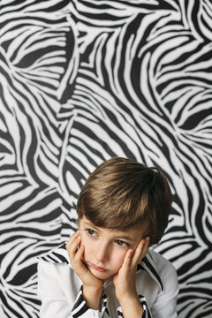 Boy holding his head with his hands in front of a zebra striped background