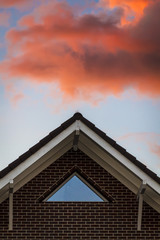 Light pink clouds in the rays of the sunset over the roof of the house.