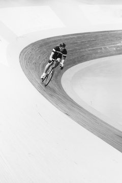 A Track Cyclist Biking Fast Through The Corner Of An Indoor Track In Black And White