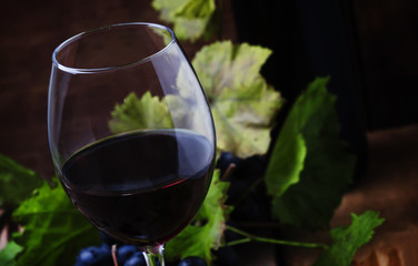 Red wine from grape varieties merlot in glass, vintage wooden background, selective focus