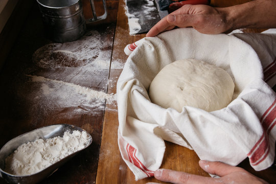 Baker's hands next to bread dough in a proofing basket