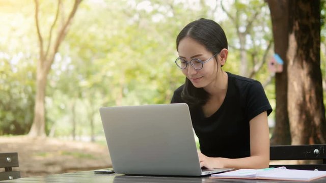 4K: Asian woman working on modern laptop in the park.