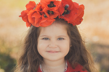 Close portrait of little child girl with big cheeks brown eyes and pout lips wearing stylish red dress with summer shirley poppy on top head