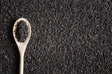Black, dried, loose tea with wooden spoon. Enjoying of tea break at the work, at home, at visit with friends, family or alone everyday. Empty place for text how to prepare a drink. Top view.