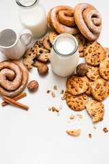 Culinary background of home-baked shop, top view free space. Wholegrain scones, baked rolls,walnuts and spices laying near bottles of milk on white table. Concept of delicious breakfast cookies