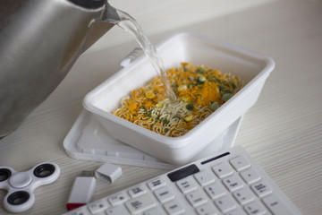 Chinese noodles on the desktop next to the keyboard. Eating instant noodles on work desk. food is on the desktop