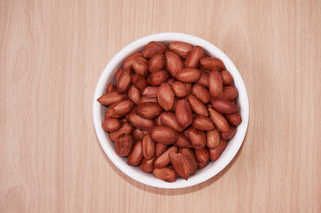 Peanuts in a white bowl. Against the background of a light tree. Top view.