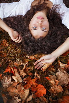 Beautiful young woman with curly hair, blue eyes and freckles lying on the leaves