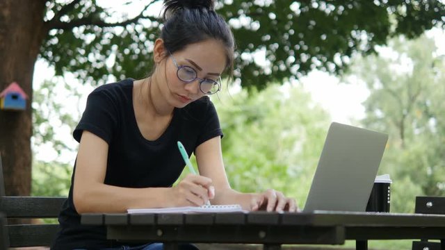 4K: Asian woman working on modern laptop in the park.