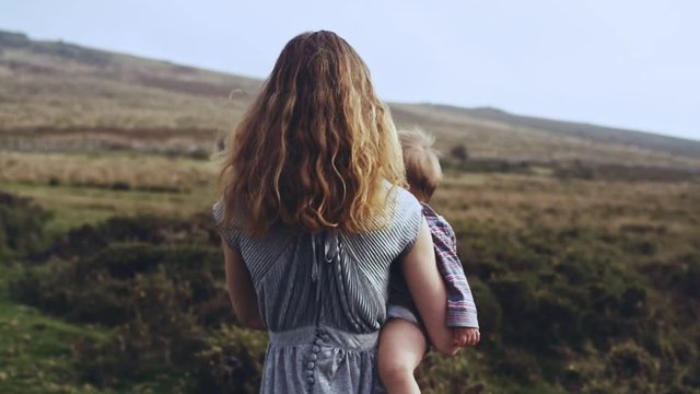 Woman in elegant dress walking on the moor in autumn with a baby in her arms
