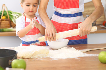 Mother and her cute daughter prepares the dough at wooden table. Homemade pastry for bread or pizza. Bakery background