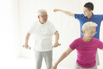 An old couple is doing dumbbell training with a trainer