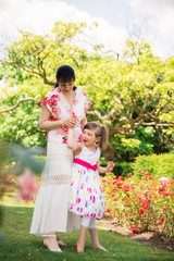 The young happy mother standing in the garden with her bewitching disabled daughter and holding her hand