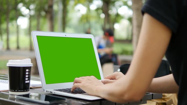 4K: Over the shoulder shot of a woman typing on a computer laptop with a key-green screen. Woman hand typing  laptop with green screen.
