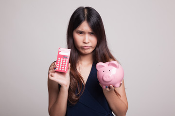 Unhappy Asian woman with calculator and piggy bank.