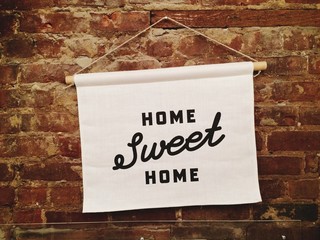 A home sweet home sign hanging on a brick wall, with handwritten type